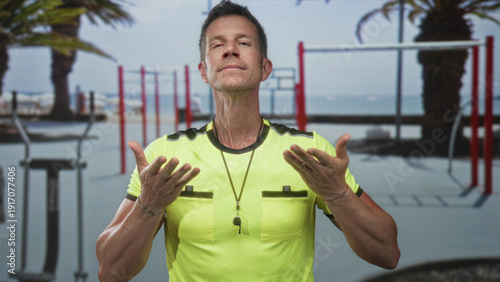 Tableau sur toile Man with palms up gesture and whistle necklace in gymnasium by outdoor calisthenics bars; calm focus