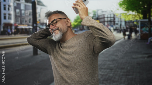 Man holding smartphone aloft with hand and smiling while dancing on a city street; joyful energy moment.