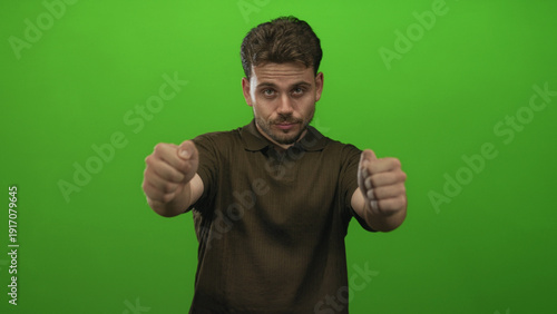 Man with hands gripping an imaginary steering wheel in a green studio, wearing brown polo shirt and focused expression; confidence driver roleplay.