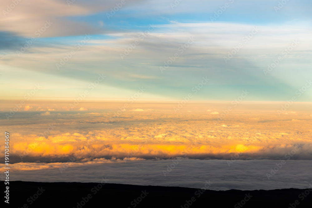 Fototapeta premium Sunset view from the summit of Mauna Kea on the Big Island of Hawaii, with volcanic slopes and clouds glowing in golden light.