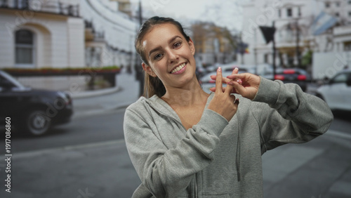 Vászonkép Woman forms hashtag with fingers on street, smiling and showing hands and nails in gray hoodie; social trend joy