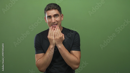 Canvas Print Young hispanic man with hands covering mouth and tense expression in green studio; nervousness uncertainty