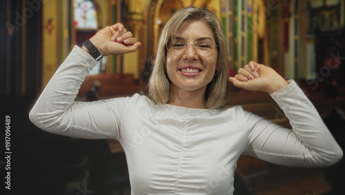 Fotografija Woman raises clenched fists inside wooden church pews under colorful stained glass windows; joy celebration