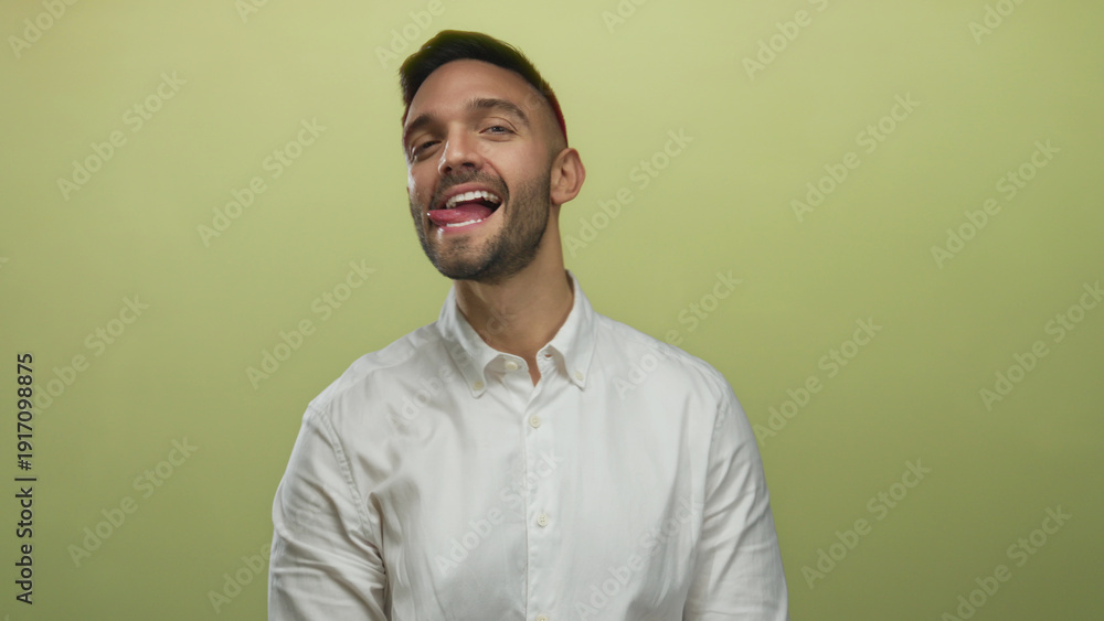 Obraz premium Young man playfully sticking his tongue out in front of a yellow background, expressing a cheerful mood.
