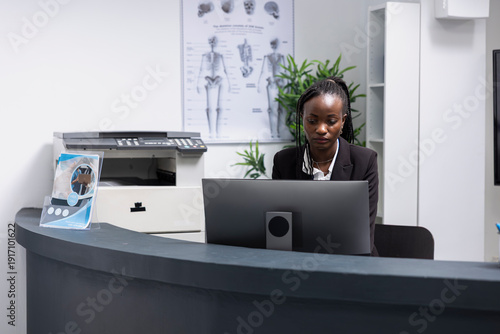 Tableau sur toile African american woman works at modern clinic reception desk, prepared to assist with patient medical appointments
