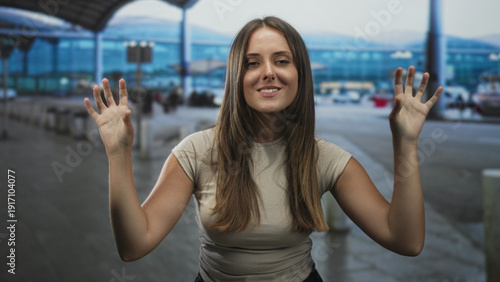 Wallpaper Mural Young woman raises hands in airport curbside terminal in playful clawing pose while smiling and showing bare hands and arms; playful welcome. Torontodigital.ca