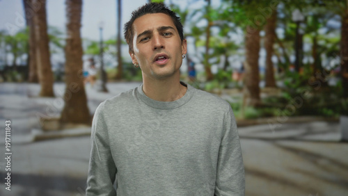 Bild auf Leinwand Young hispanic man flipping middle fingers in park amid palm trees with scowling expression; defiance