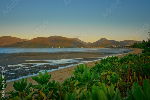 Wallpaper Mural Tropical beach near Cairns, Australia at sunset, sandy shore, calm sea, coastal vegetation foreground, mountain range background, golden evening light, Queensland coastline landscape Torontodigital.ca