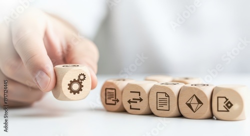 Wooden cubes featuring workflow diagram icons being set by hand using macro sharpness and soft white blur behind.