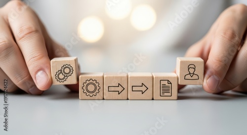 Wooden cubes featuring workflow diagram icons being set by hand using macro sharpness and soft white blur behind.