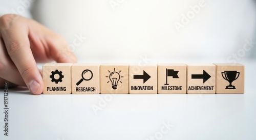 Wooden cubes showing strategic timeline icons arranged by hand using shallow depth and calm white gradient background blur.