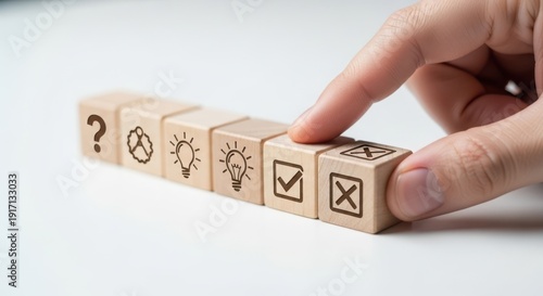 Decision making icons on wooden cubes being aligned by hand using cinematic shallow focus and white background blur effect.