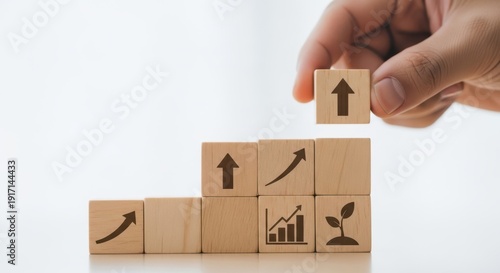 Strategic growth icons on wooden cubes arranged by hand with realistic depth of field and subtle white background blur.
