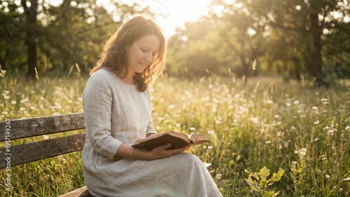 Woman Reading Bible on Bench in Meadow at Sunset