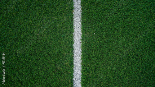 Top down view of a soccer field featuring a detailed grass texture and a bold white sideline. The image showcases close up green turf with visible blades.