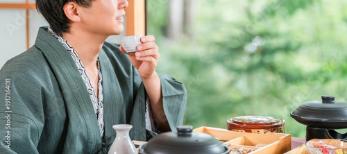 Fotografi Young Asian man drinking sake with kaiseki cuisine at a ryokan (room dining, kai