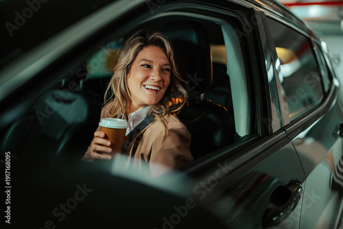 Photography Happy woman is seated in her car after work, enjoying a take away coffee and loo