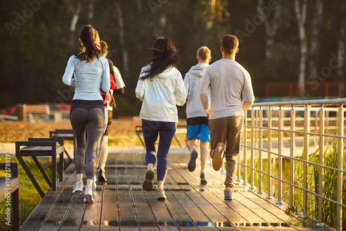 Foto Running group of young athletes jogging marathon in park, healthy outdoor fitness workout of male and female runners