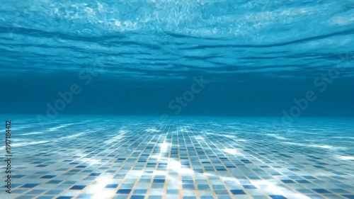 Underwater view of a tiled pool with clear blue water and sunlight reflection.