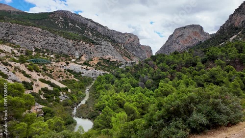 Handheld POV walking sideways right on the Caminito del Rey boardwalk, showcasing the steep limestone cliffs and pine trees of the Gaitanes Gorge in Malaga.