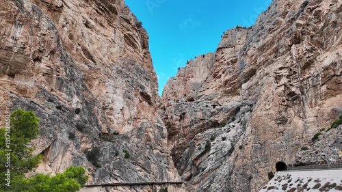 A handheld POV walking sideways right along the cliffside boardwalk, tilting the camera from the high rock peaks down to the center of the gorge path in Malaga.