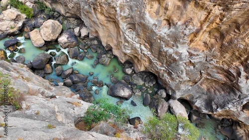 A handheld POV walking sideways right along the cliff edge, looking directly down at the turquoise river and rocky bottom of the Gaitanes Gorge in Malaga.