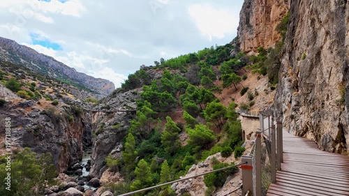 A handheld POV walking forward on the iconic wooden path of Caminito del Rey, showing the steep rock face and the scenic mountain valley of Malaga.