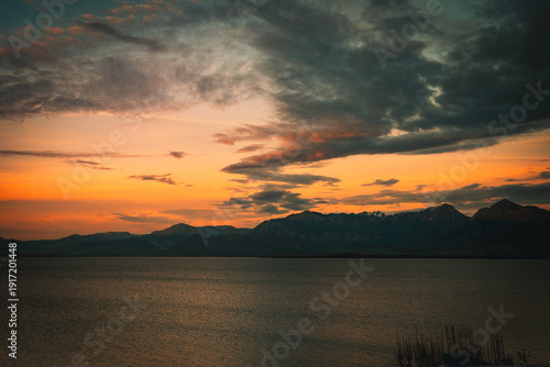Scenic sunset over Lake Skadar in Montenegro with dramatic mountain silhouettes and orange clouds at twilight.