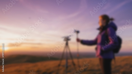 Wallpaper Mural Blurred background of 	Sustainability student checking wind direction instrument and handheld anemometer on a high windy hilltop, vast open grassland stretching endlessly with dramatic sunset sky. Torontodigital.ca