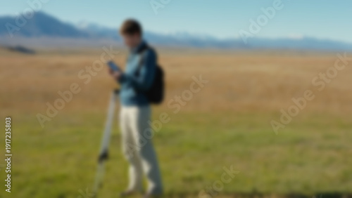 Wallpaper Mural Blurred background of Environmental research student measuring air quality with a handheld digital device, standing in an open grassy plateau, distant mountain range under clear sky background, noon. Torontodigital.ca