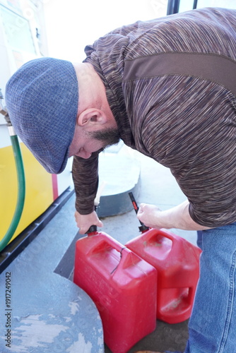 Foto A man in a flat cap and casual outdoor wear filling red plastic portable gas canisters at a gas station pump