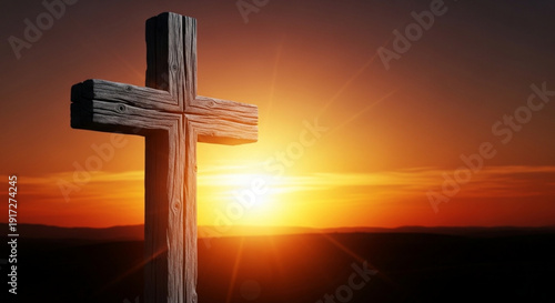 Wooden cross silhouette against vibrant orange sunset with radiant sunbeams and dark landscape background symbolizing faith and spirituality
