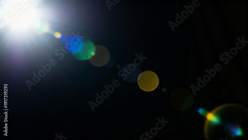 White lens flare light from corner on dark background with soft color circles