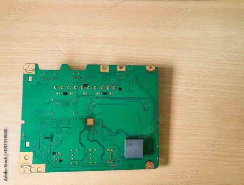 Green printed circuit board with electronic components on a wooden table background.