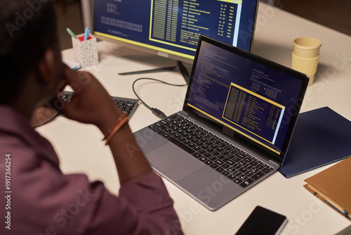 Software engineer analyzing terminal output on laptop and external monitor, reviewing logs and system code in a professional office environment

