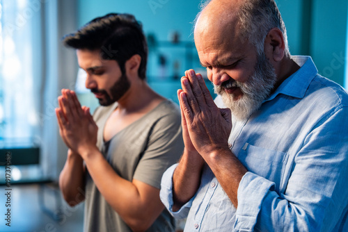 Indian senior dad and adult son performing Hindu prayer ritual indoors with folded hands