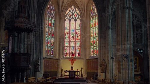 Wide symmetrical cathedral interior in Bordeaux with pews altar cross and stained glass 