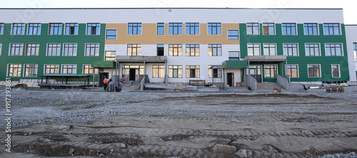 Final stage of new school construction in a modern residential district, with workers on site. Urban development project in progress, contemporary building. Ust-Kamenogorsk, Kazakhstan