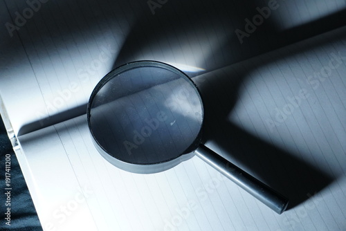 Foto A magnifying glass is placed on an open notebook under a cool blue spotlight, creating a sense of professional investigation and deep analytical research