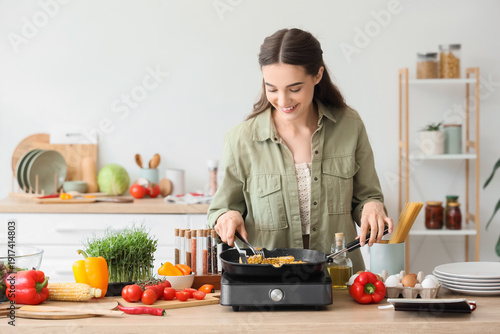 Young woman frying corn on grill pan in kitchen