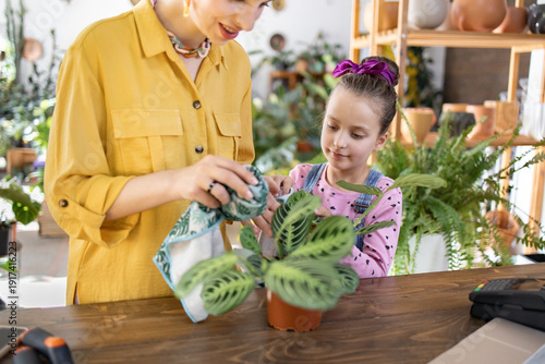 Canvas Print A woman and a young girl are shown caring for a potted houseplant, creating a he