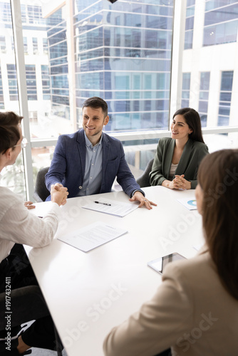 Bild auf Leinwand Business professionals gathered around modern conference table in corporate office, starting negotiating with handshake gesture between two men leaders