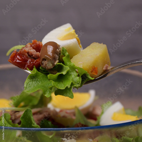 Primo piano di cucchiaio con lattuga, patata, pomodoro, oliva e tonno