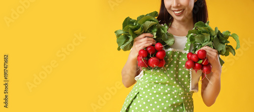 Young housewife with ripe radish on yellow background, closeup