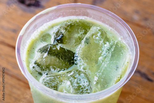 Close up of a Iced Matcha or Green Tea in Plastic Glass, High Angle View. Wooden table and place for text.
