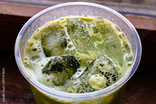 Close up of a Iced Matcha or Green Tea in Plastic Glass, High Angle View. Wooden table and place for text.
