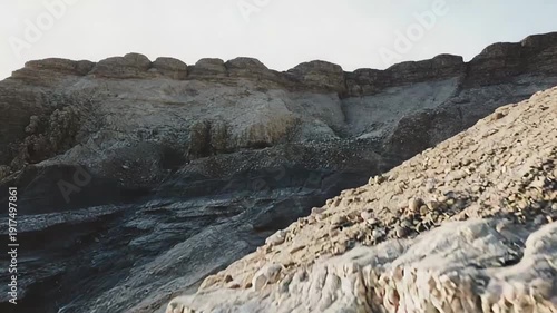 Arid desert landscape revealing layers of ancient geological rock formations, with rough stone textures and natural patterns carved by centuries of wind and water erosion