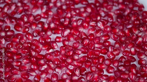 Macro shot of scattered pomegranate seeds against white background. Closeup image of radiant red pomegranate arils showcasing translucent texture and juice droplets