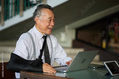 Senior businessman working on a laptop with his arm in a sling