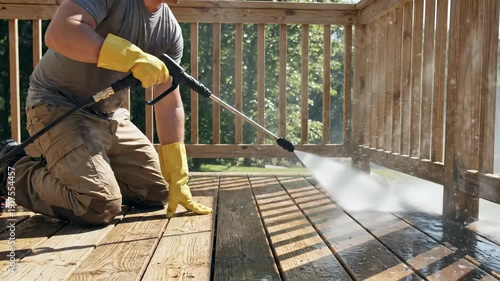 Person cleaning dirty wooden deck with power washer, removing grime from outdoor patio planks, home maintenance
